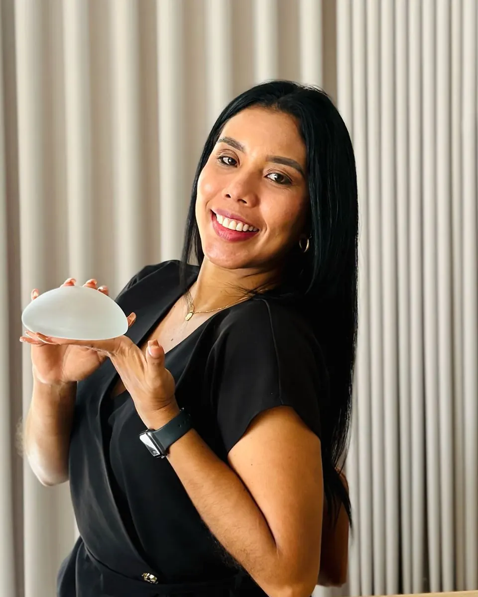 Eileen, Experiences Coach at Dr. Fulvio Correa's practice in Cartagena, smiling in a black top and holding a breast implant sizer